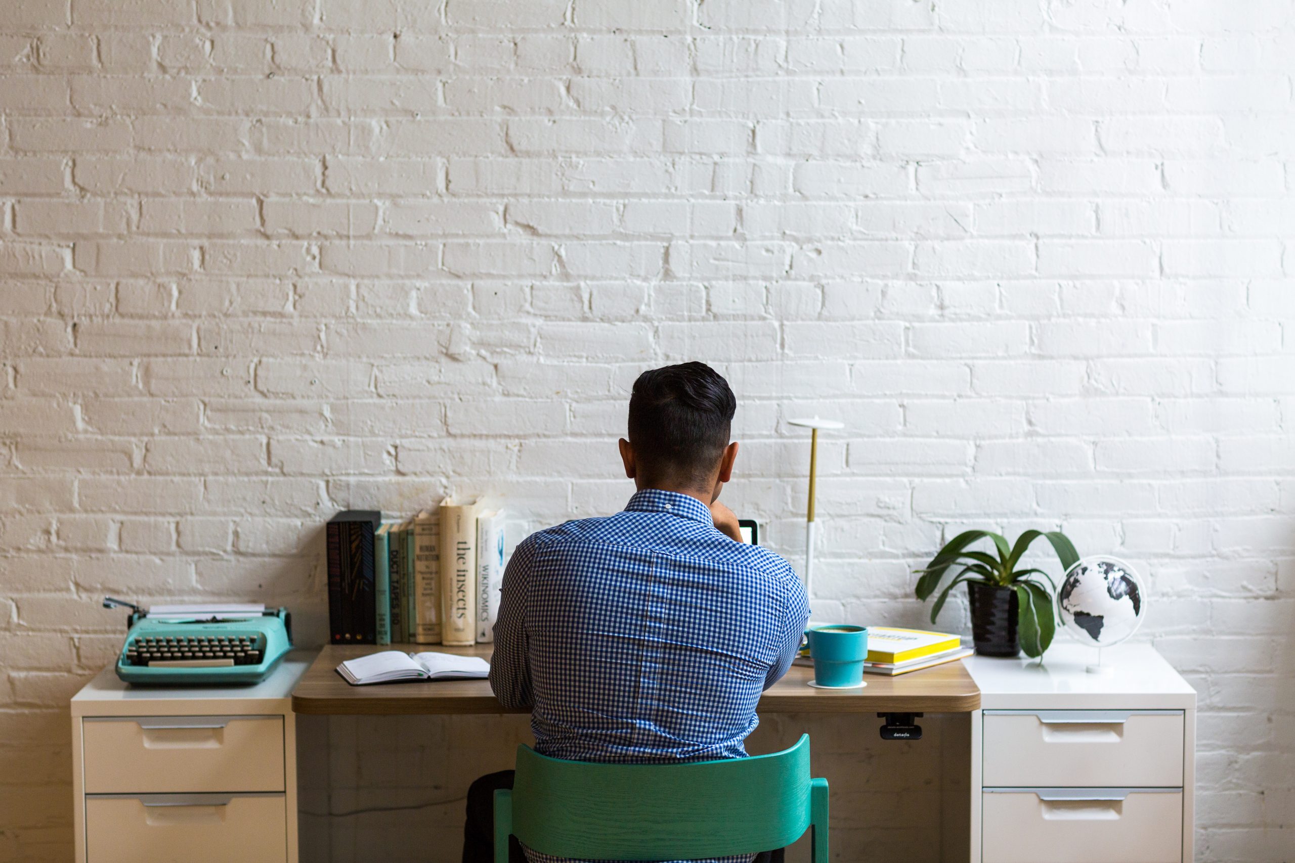 Man working at a desk facing a white brick wall