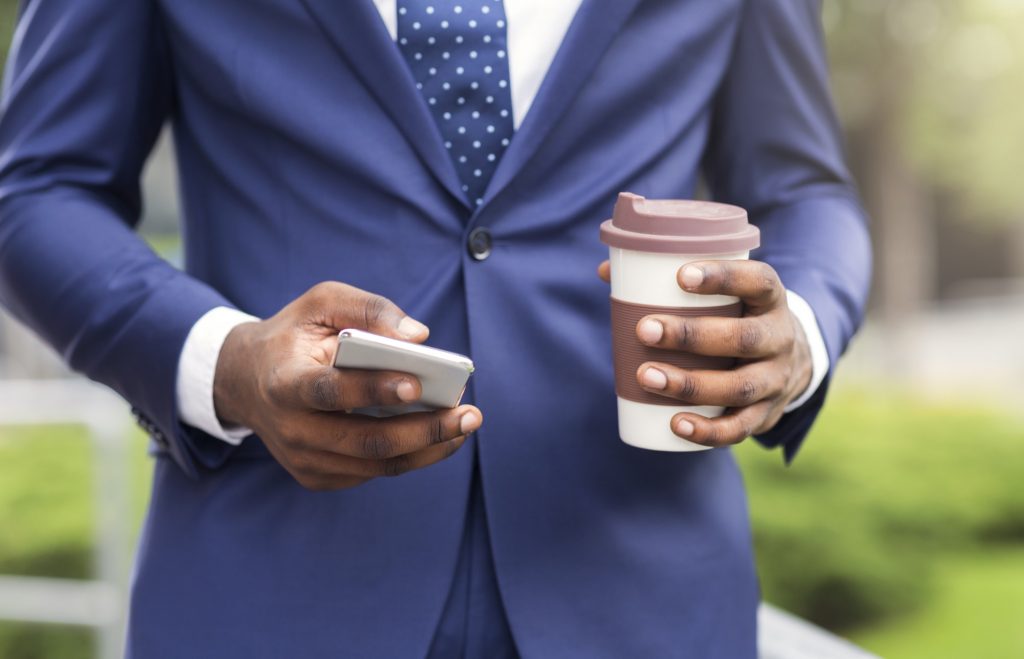Waist level image of a man in a blue suit holding a cup of coffee and a cellphone