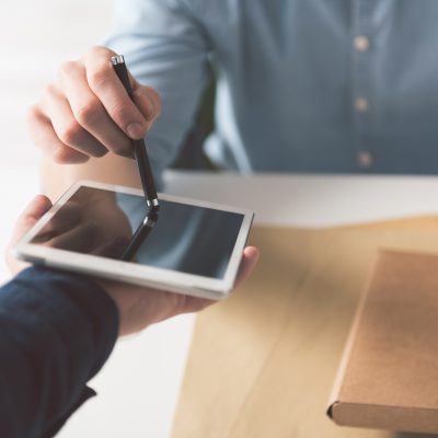 Electronic sign. Close-up of stylus in hand of guy and digital screen in hand of courier. Male is holding box and putting his signature after accepting delivery